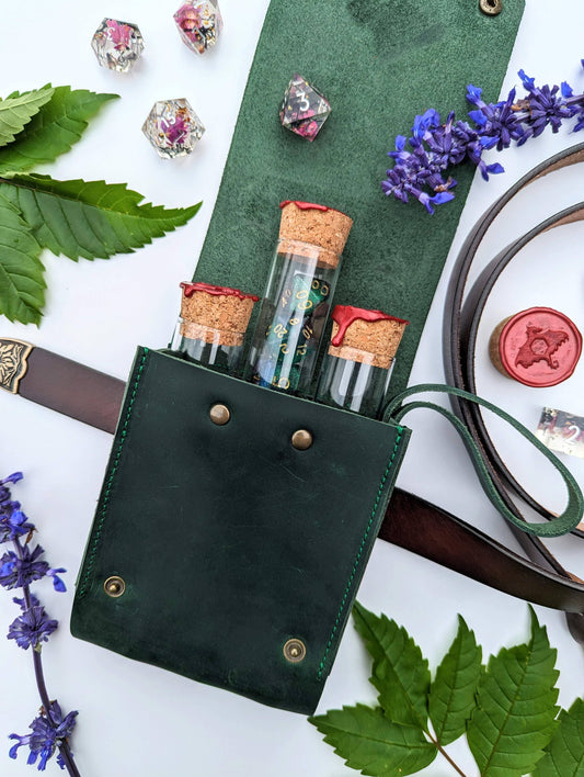 A green genuine leather pouch with a built-in belt loop and snap closures, designed to hold glass vials with dice inside, displayed with flowers and leaves around it.